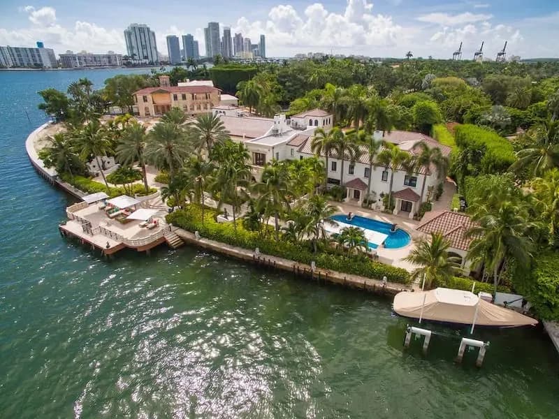 Aerial view of a waterfront Miami mansion with palm trees and a private dock