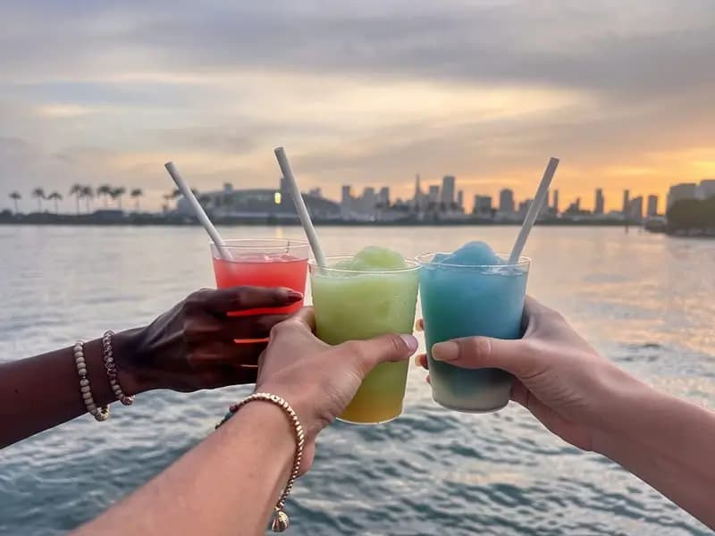 Friends toasting frozen cocktails with the Miami skyline at sunset